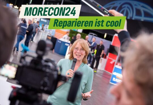 Tabea Rößner steht mit einem Mikrophon auf der MORECON Messe uns spricht in eine Kamera. Copyright Oliver Nimz